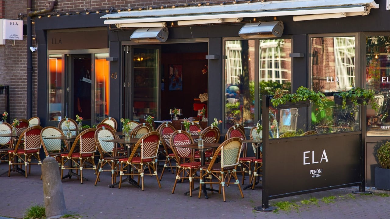 Outside full frontal view of the Ela Restobar terrace, with wooden tables decorated with flowers.